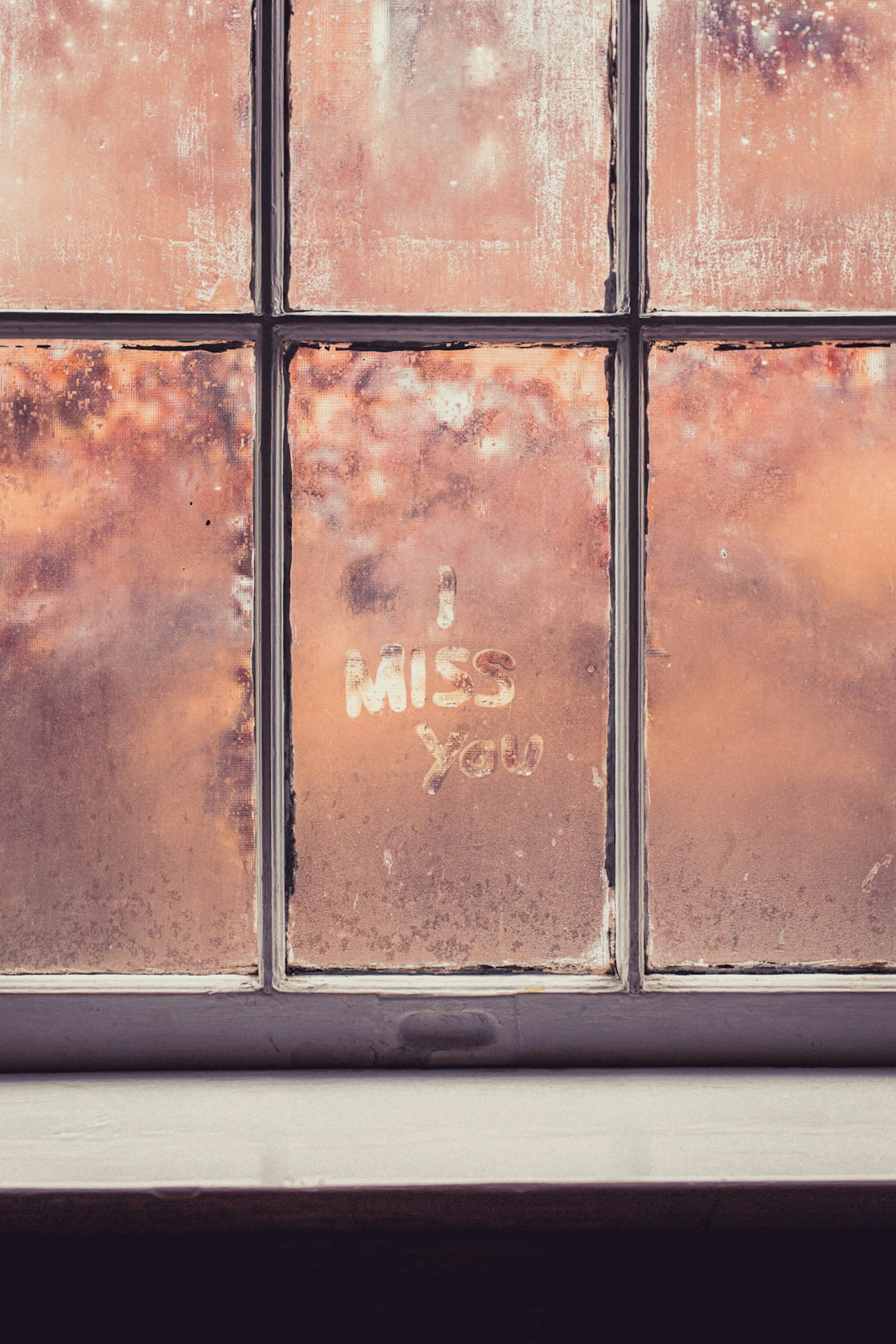 The words 'I miss you' are written in a window's condensation.