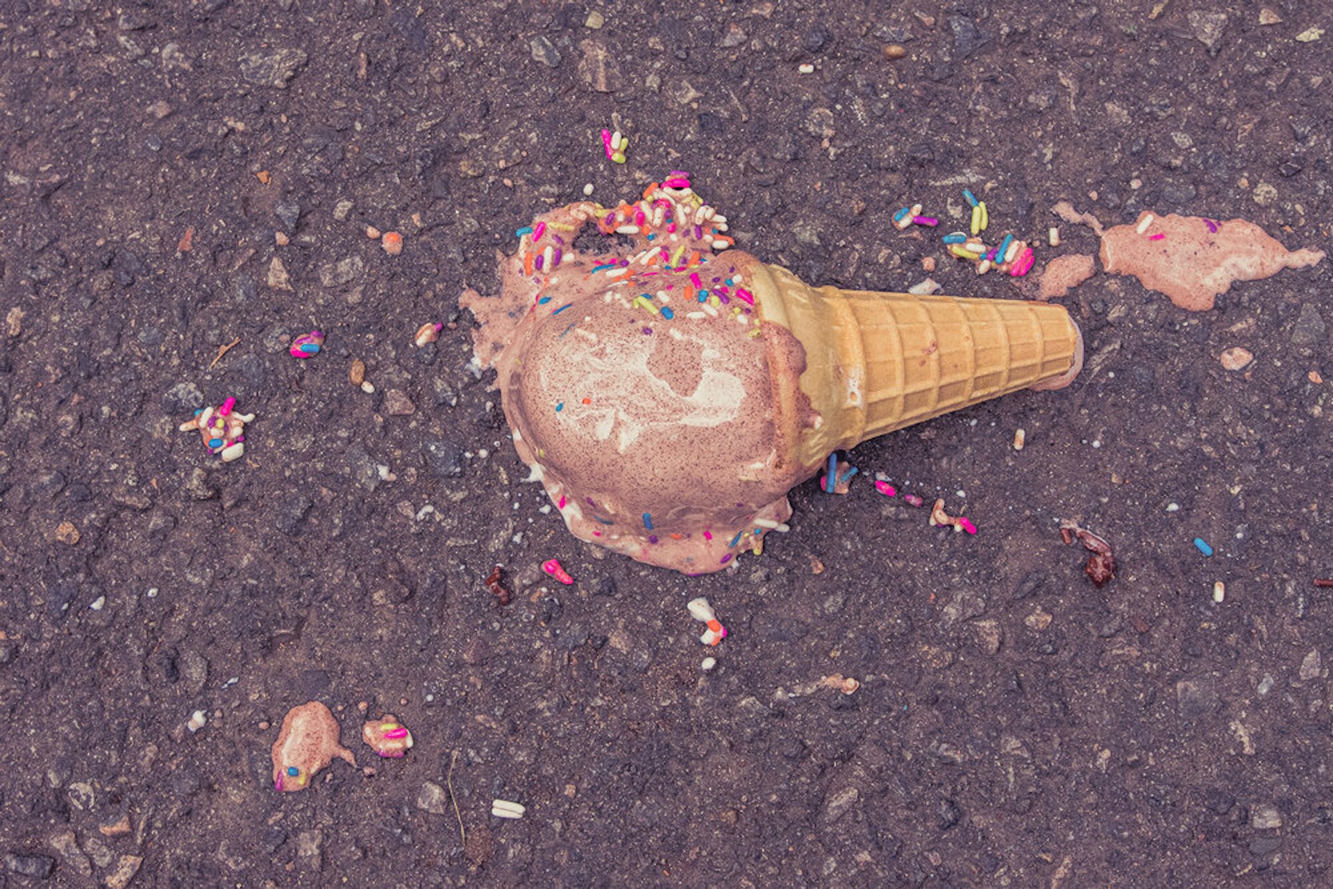An ice cream with sprinkles that has fallen on the pavement.