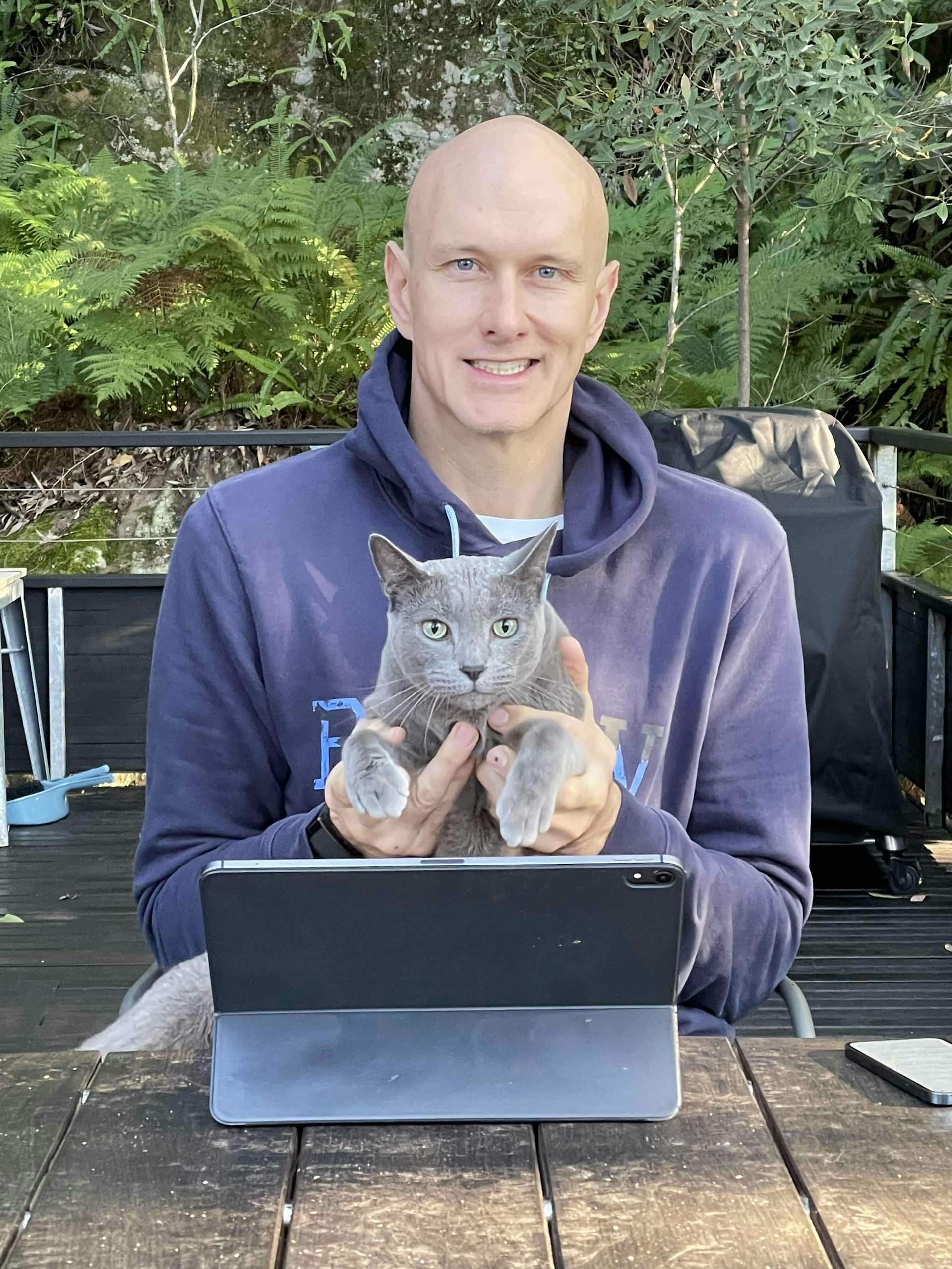 Brendan smiles at the camera, holding a grey cat in his hands.