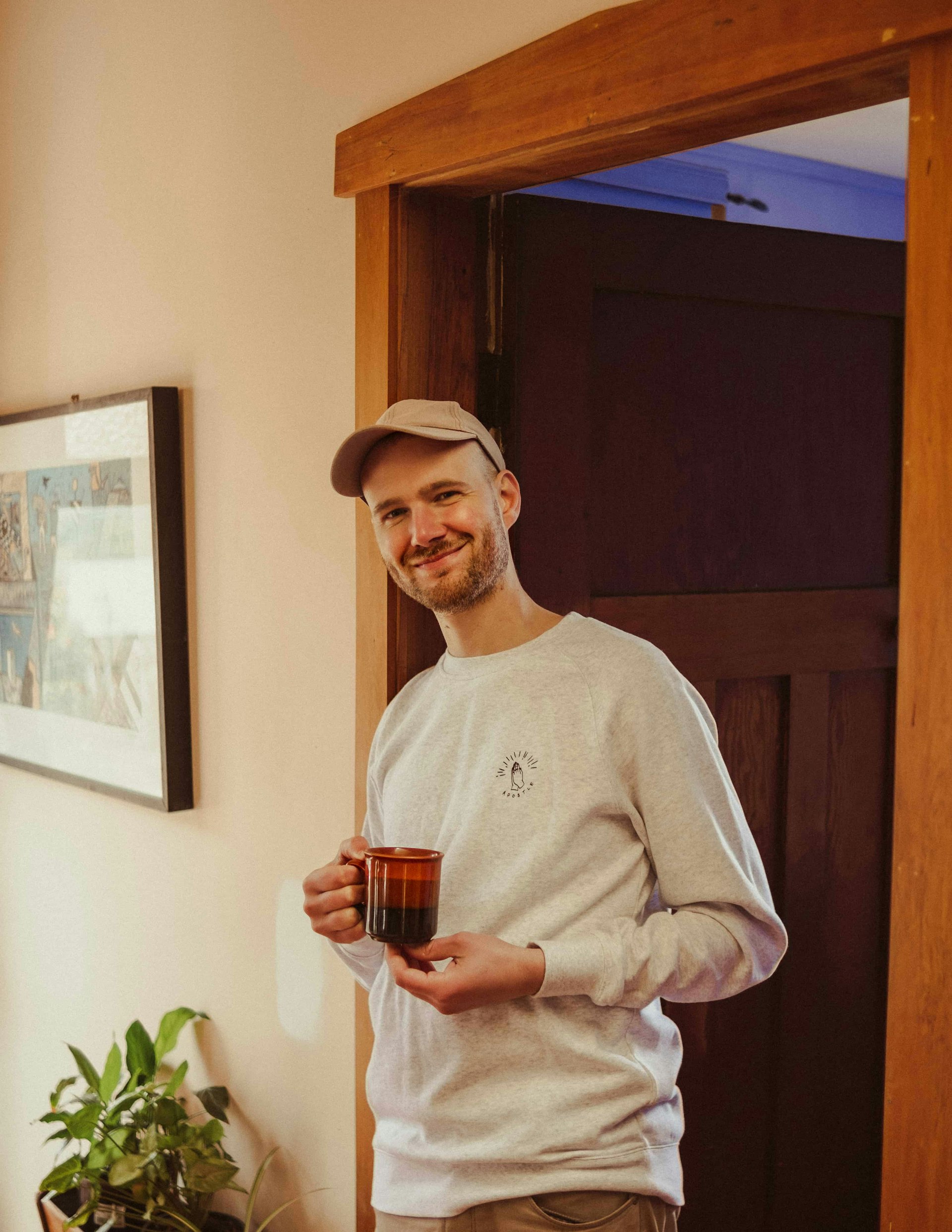 Mat stands smiling in a doorway, holding a mug.