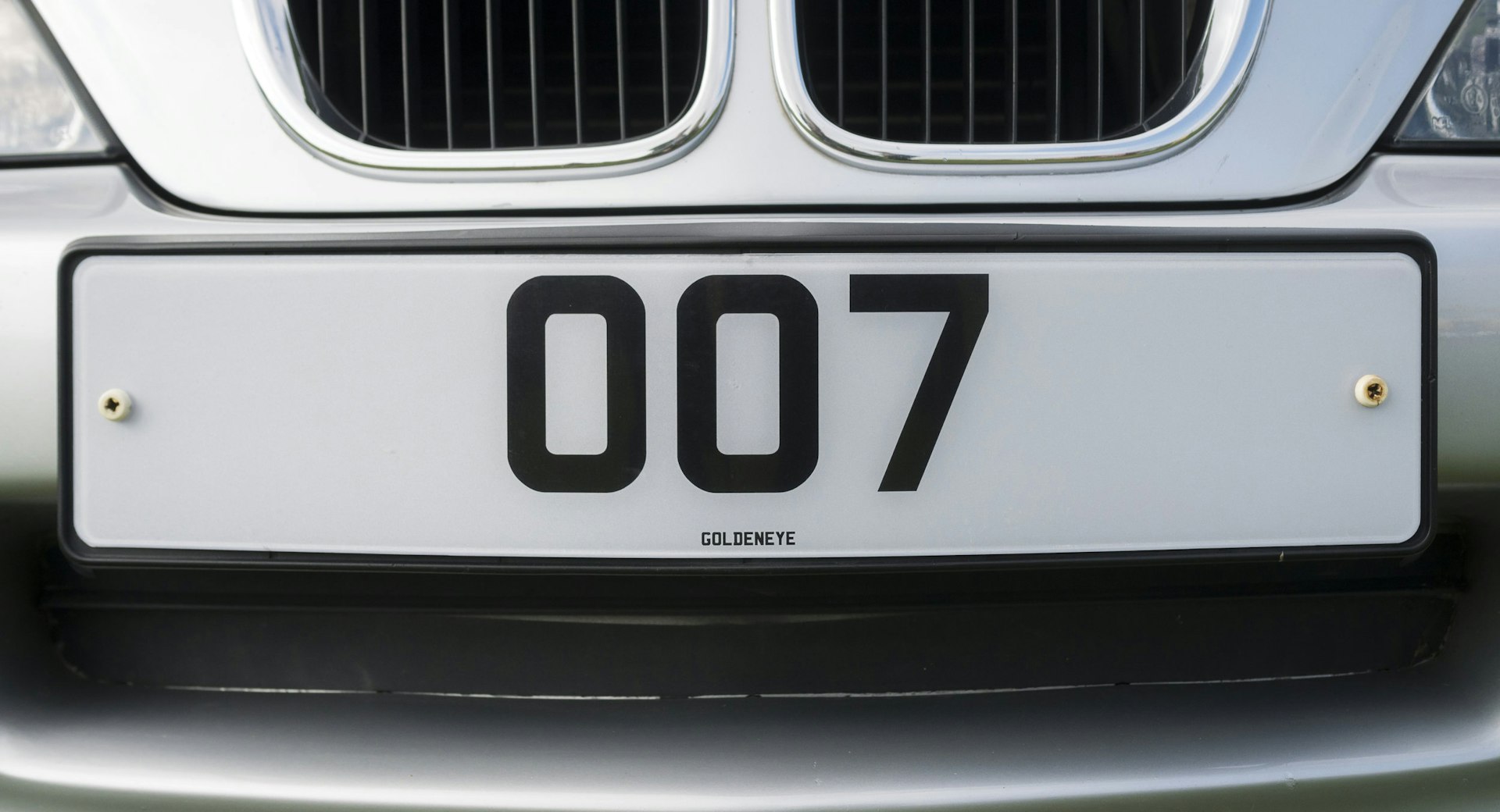 A close-up shot of a license plate on the front of a silver car that has the license plate number 007. 