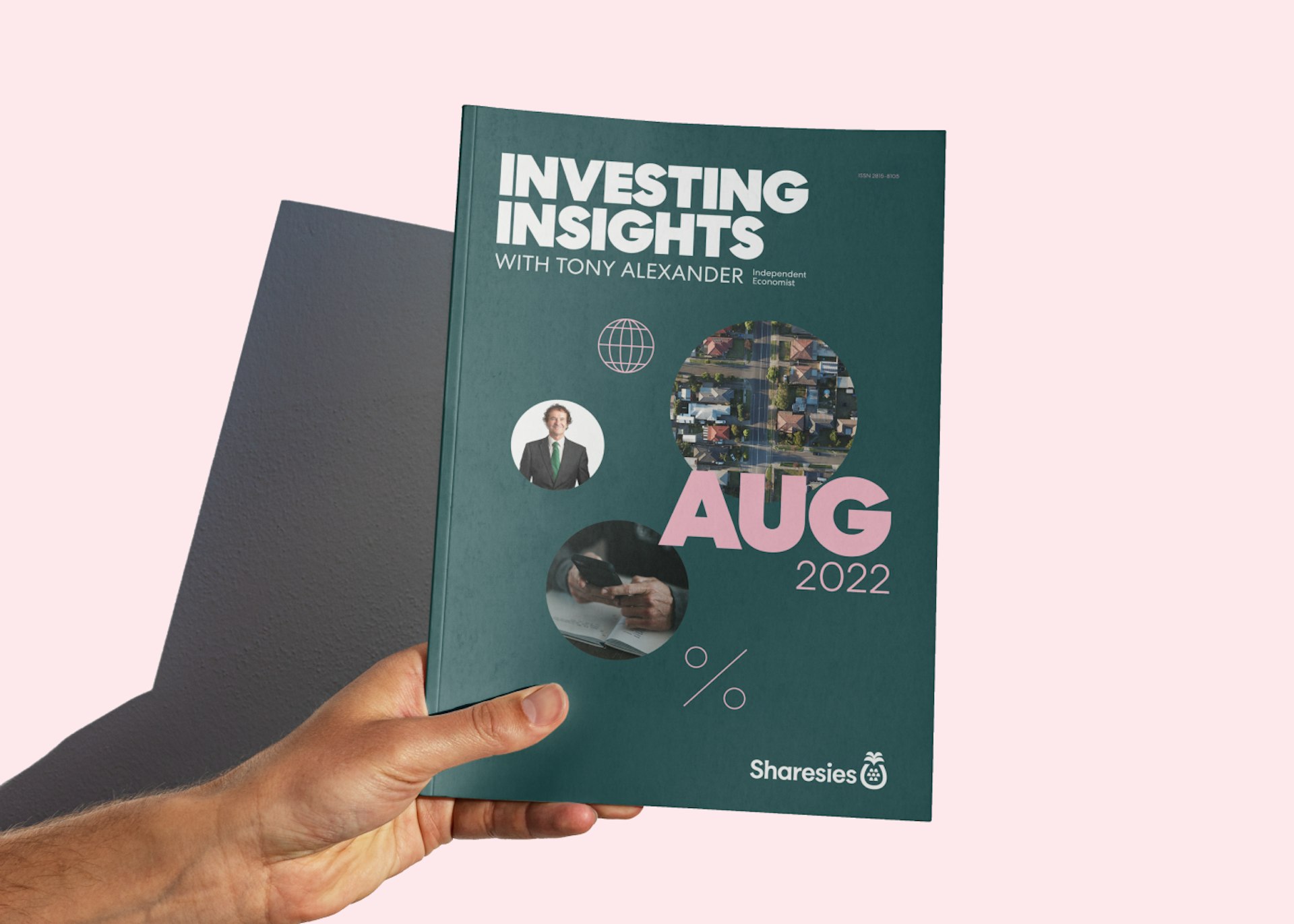 A picture of a hand holding a physical copy of Tony Alexander's Investing Insights report for August 2022, in front of a solid light pink background. 