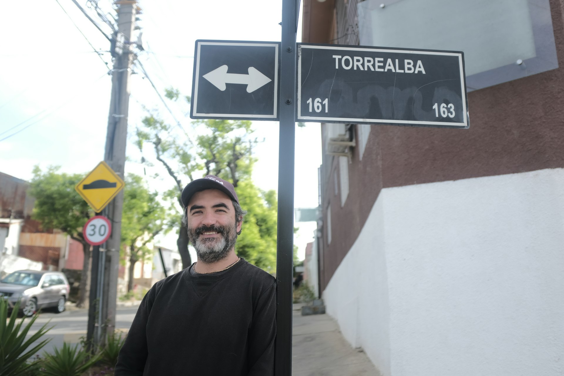 A smiling Armando stands under a street sign that reads 'Torrealba'. 