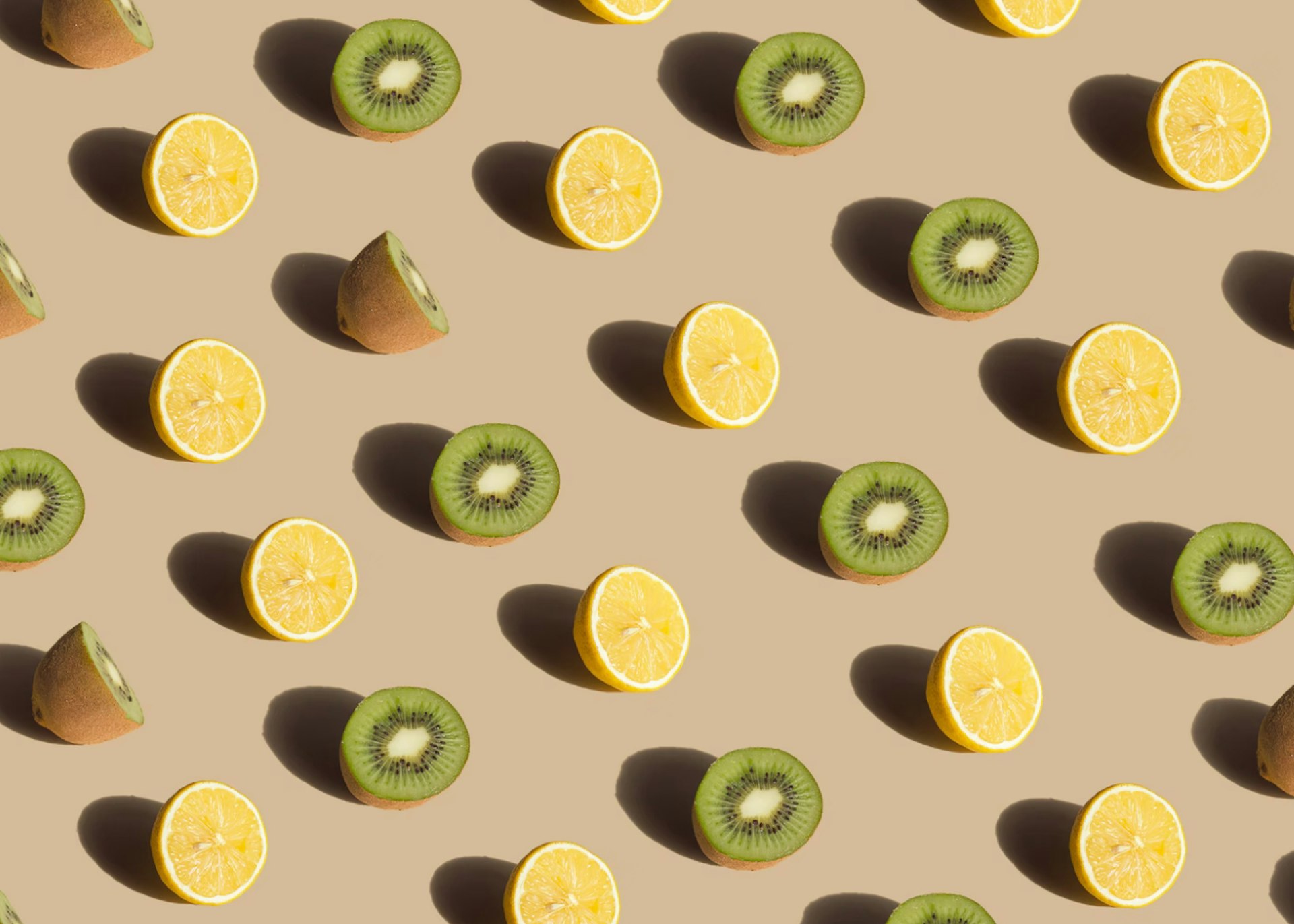 Rows of sliced kiwifruit and lemon against a beige background. 