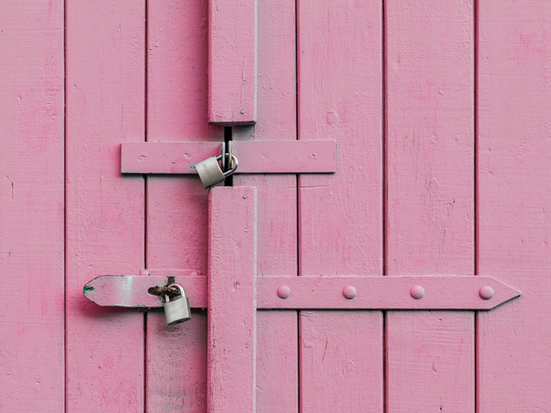 A pink wooden door secured by two silver padlocks. 