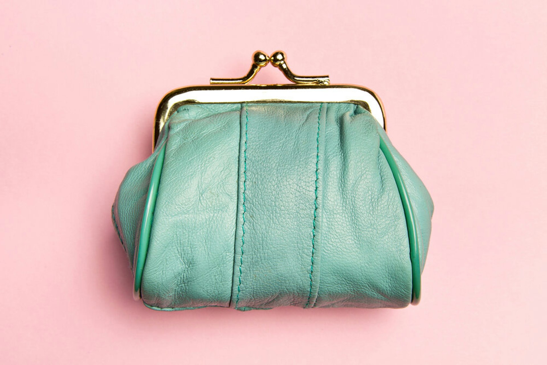 A green leather purse on a pink background