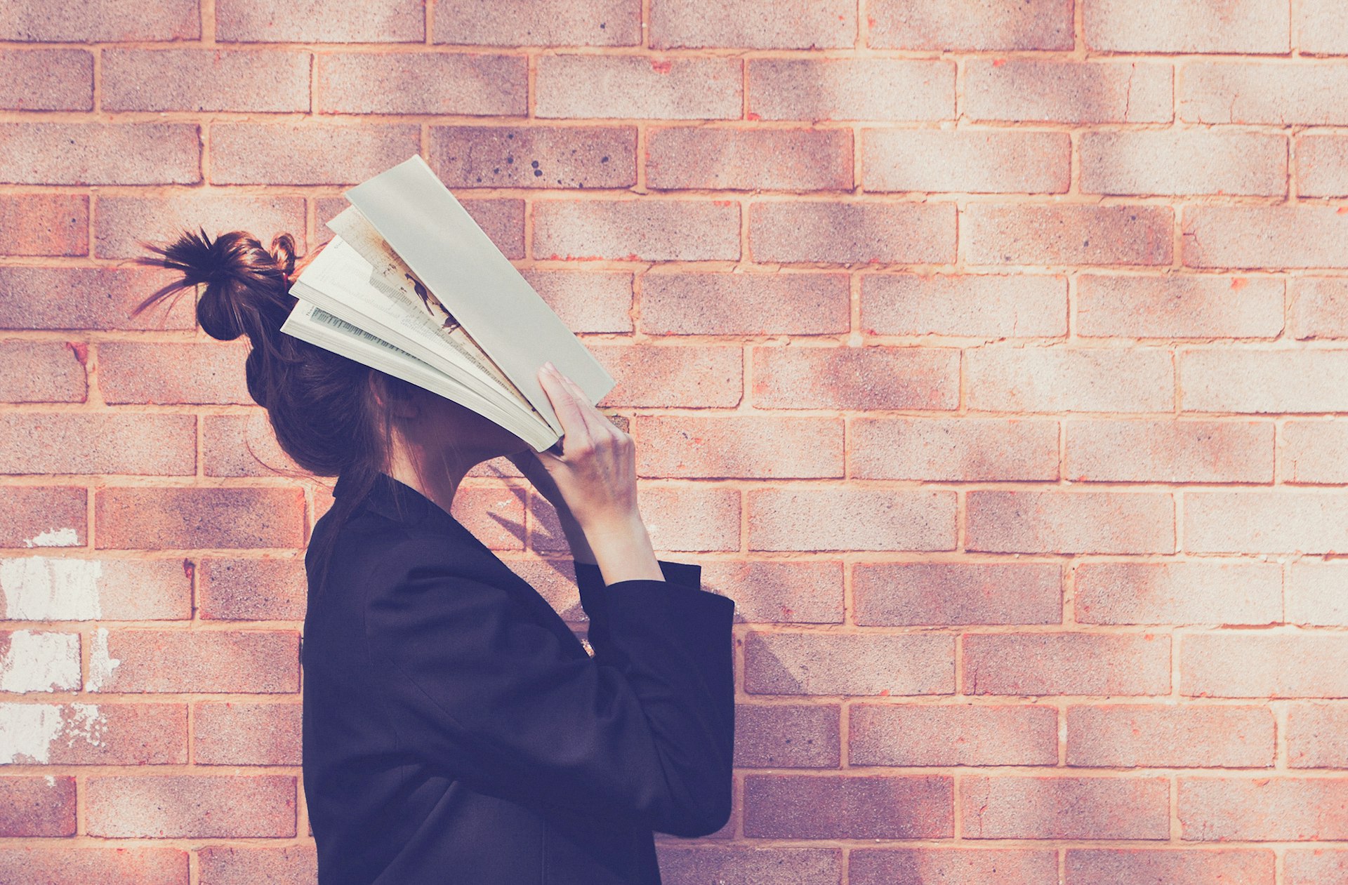 A woman standing in profile with a book spread over her face.