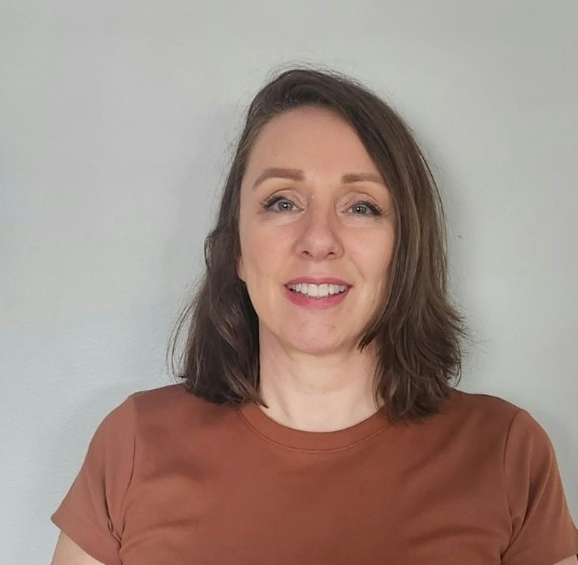 A woman with brown hair wearing a brown t-shirt smiling at the camera