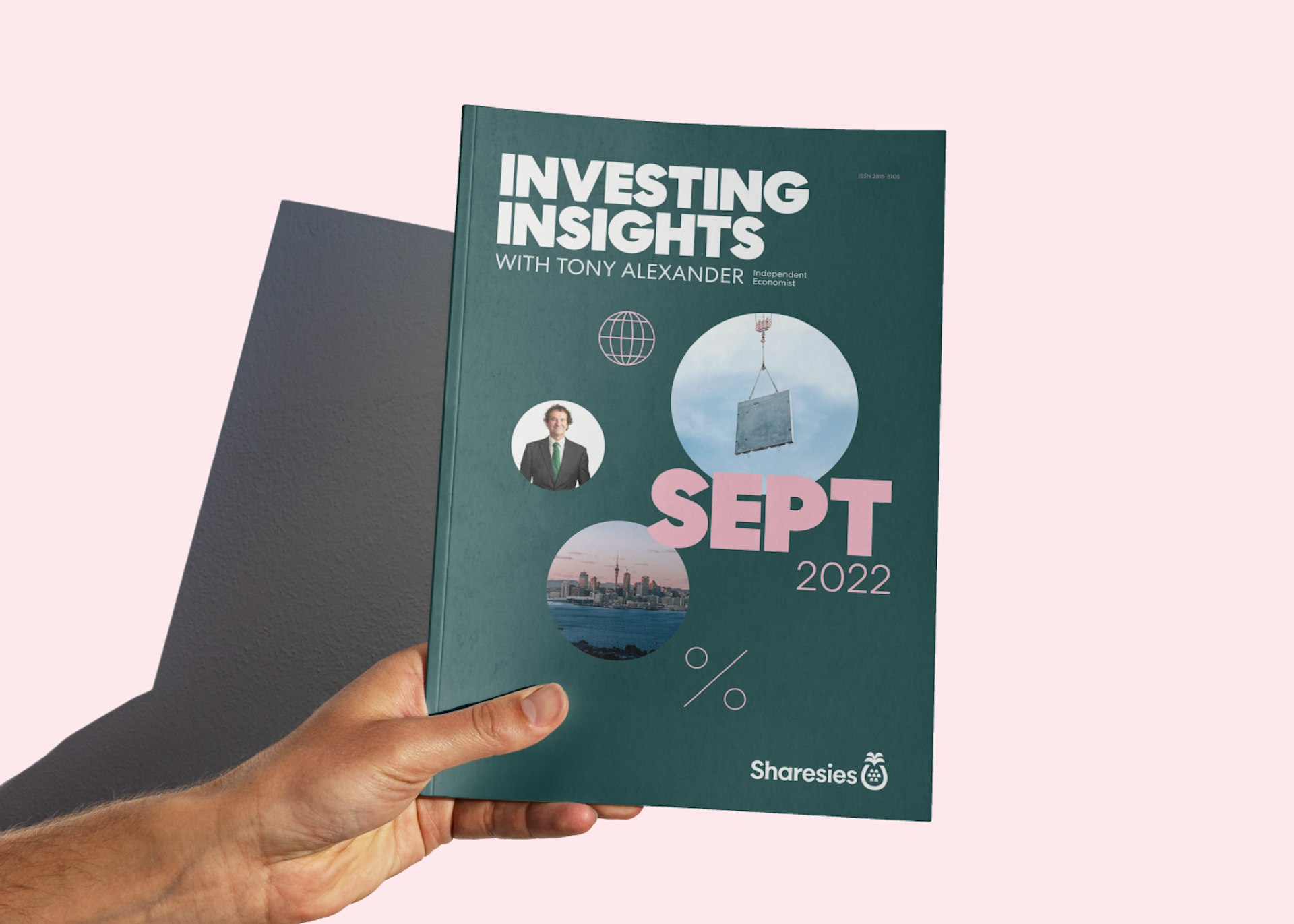 A photo showing a hand holding a physical copy of Tony Alexander's Investing Insights report for September, in front of a solid pink background.  