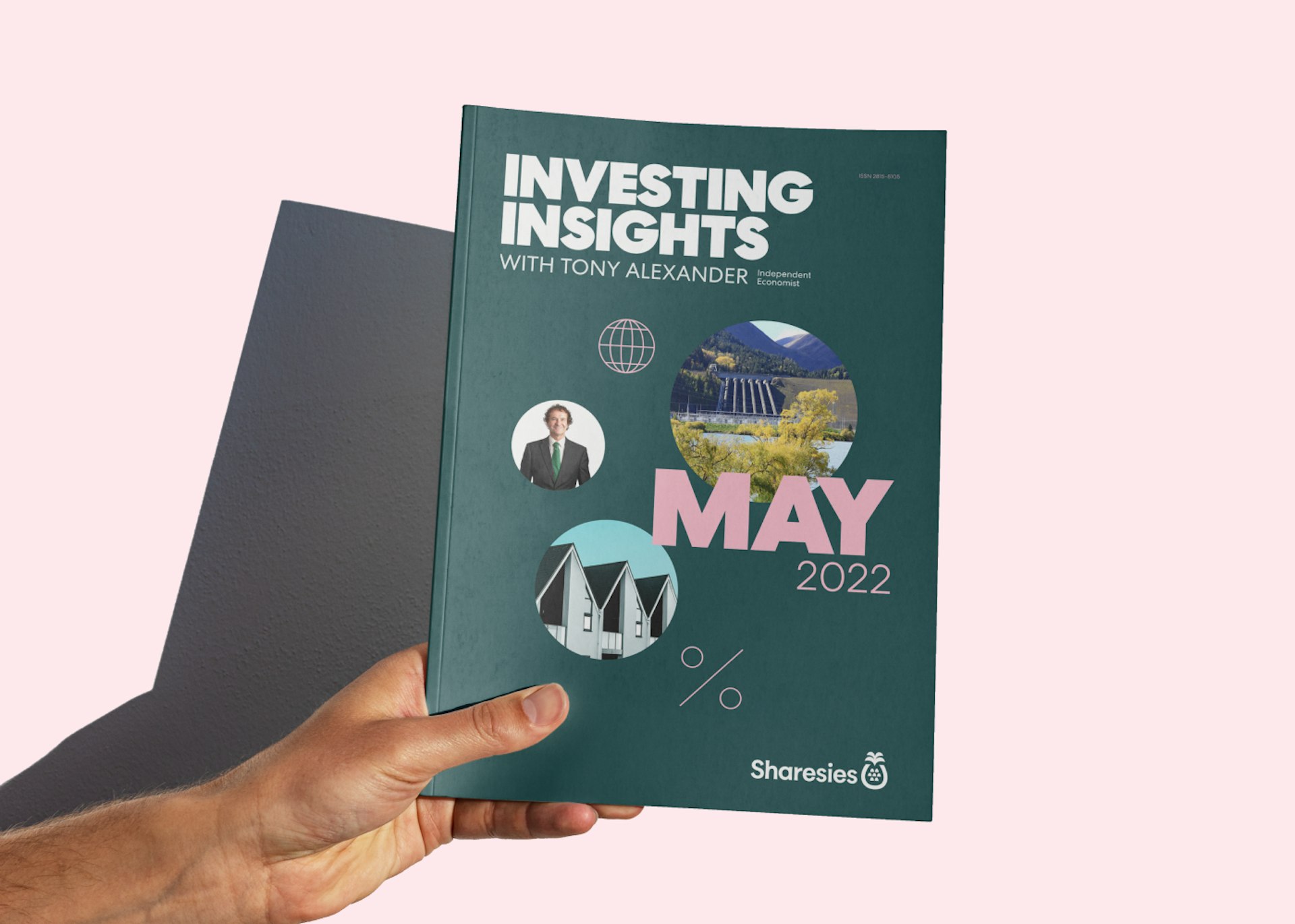 A hand is holding a printed copy of May 2022's edition of Investing Insights with Tony Alexander against a pink wall, with a shadow of the hand and report being cast to the left. 