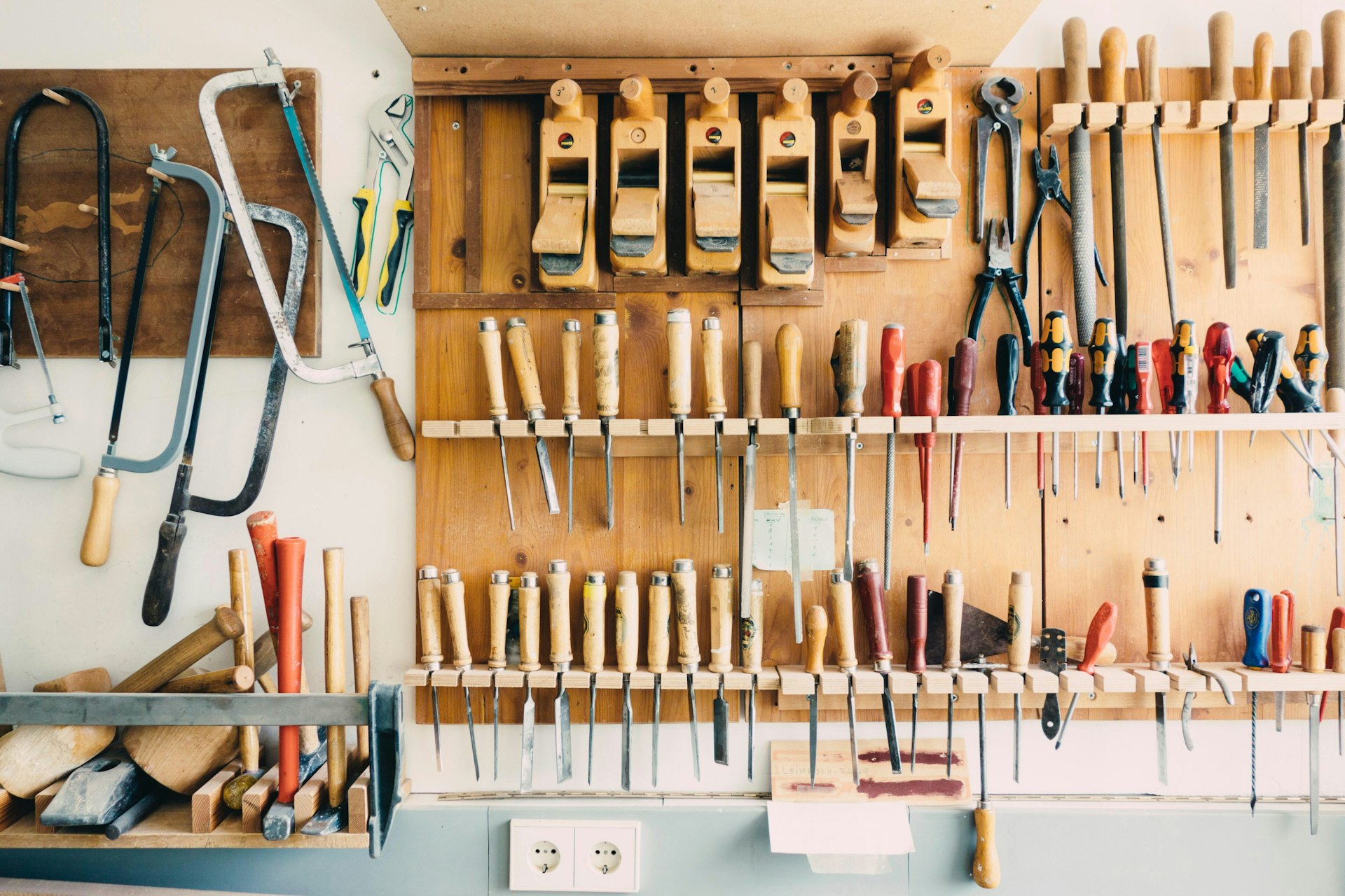 A couple rows of DIY tools hanging up on a wooden wall