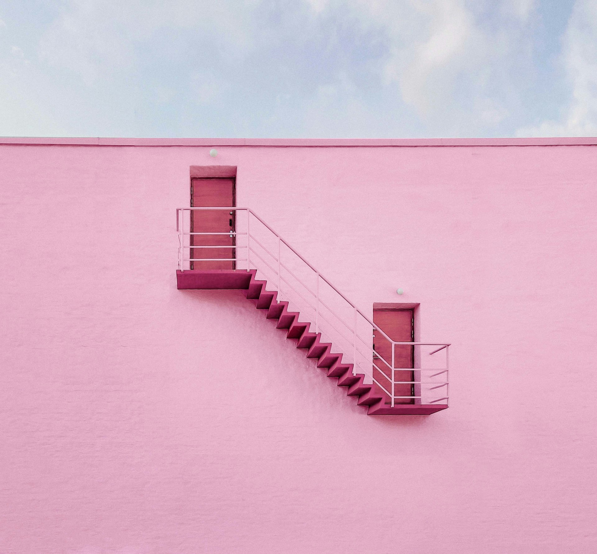 A stairwell leads between two doors on a pink wall.