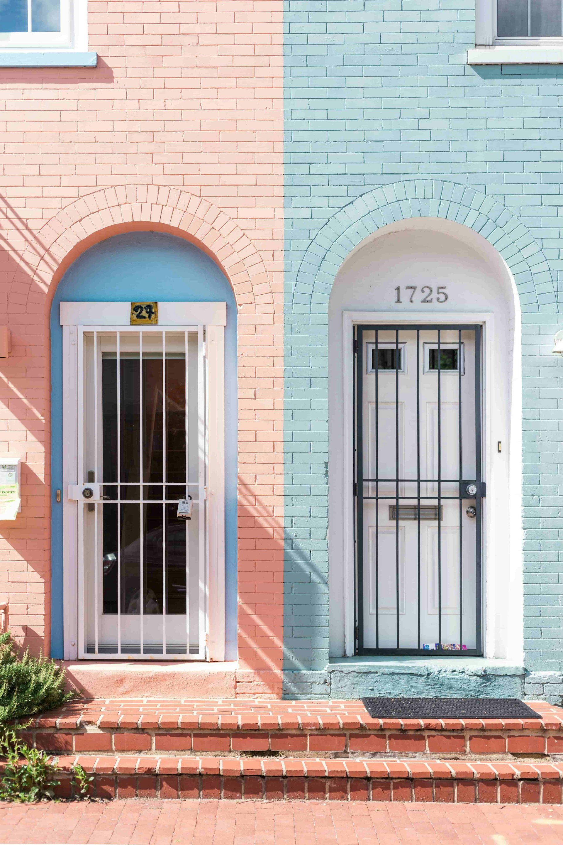 Two white doors against a blue and pink brick wall.