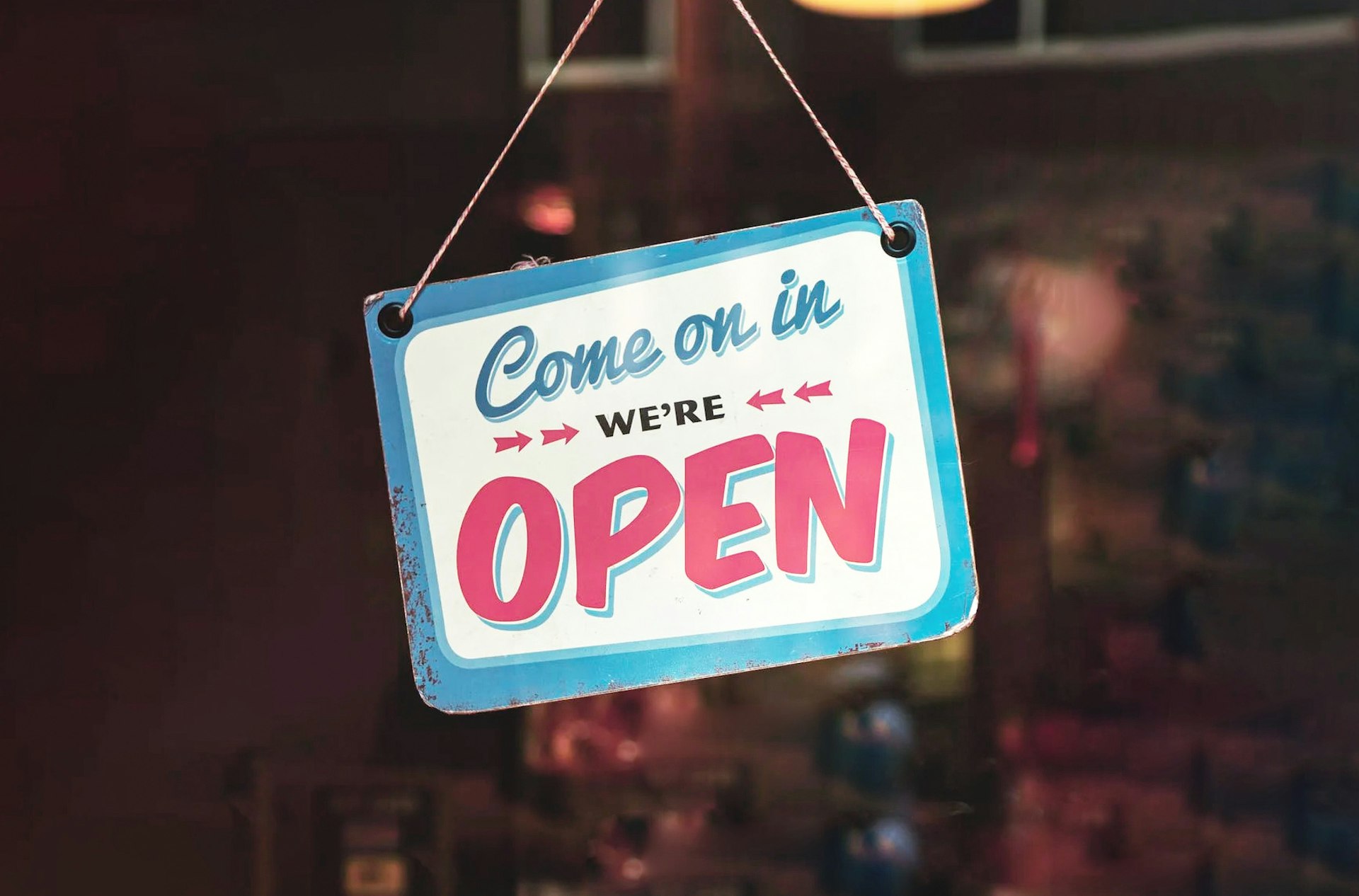 A sign hanging in a doorway that says 'come on in, we're open'.